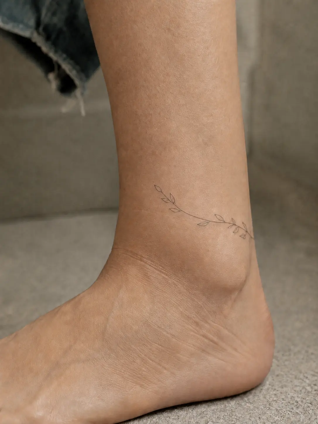 Tatouage discret en forme de branche sur une cheville